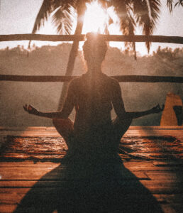 Zdjęcie odwróconej tyłem kobiety medytującej w blasku słońca.