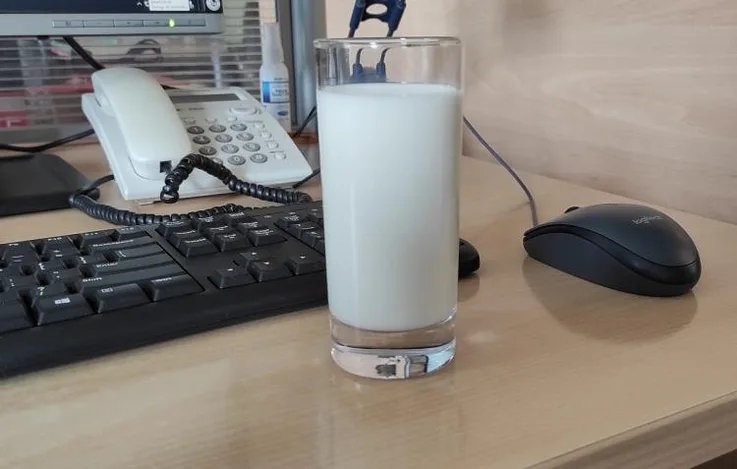 Zdjęcie szklanki mleka postawionej na blacie obok klawiatury komputera.