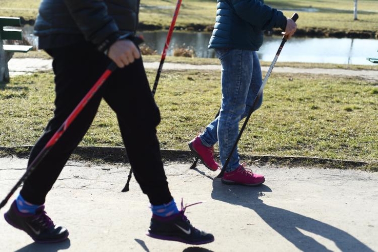 Zdjęcie dwojga seniorów od pasa w dół uprawiających nordic walking.