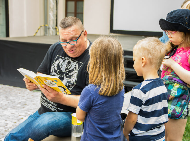 Zdjęcie czytającego mężczyzny i dzieci zgromadzonych wokół.